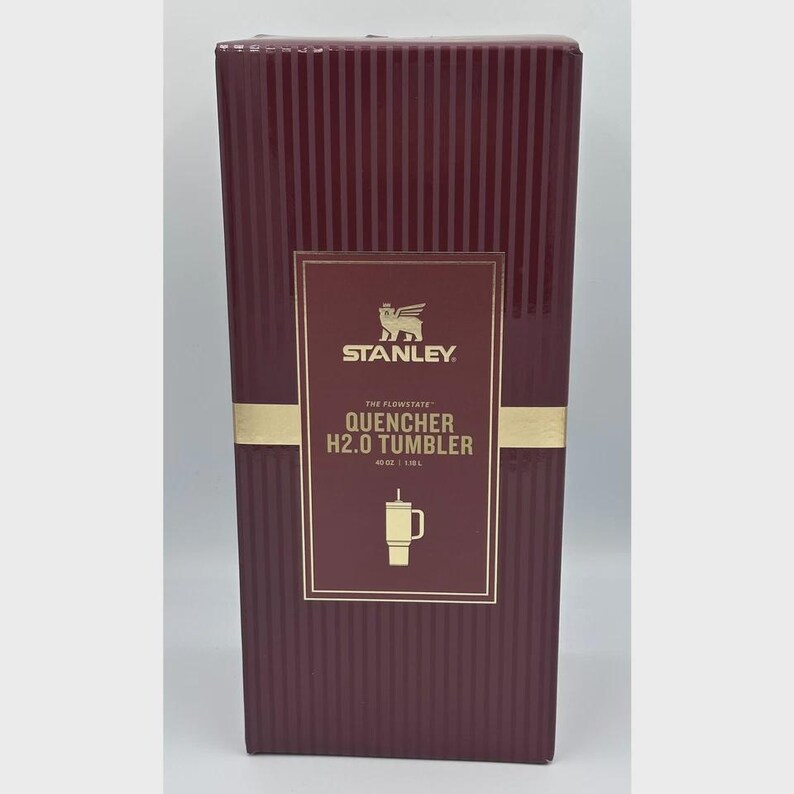 Peut inclure: Bo&icirc;te de gobelet Stanley Quencher H2.0 de couleur bordeaux. La bo&icirc;te pr&eacute;sente des lignes verticales et une &eacute;tiquette rectangulaire dor&eacute;e avec le logo Stanley et les d&eacute;tails du produit. Le gobelet contient 1,18 L.