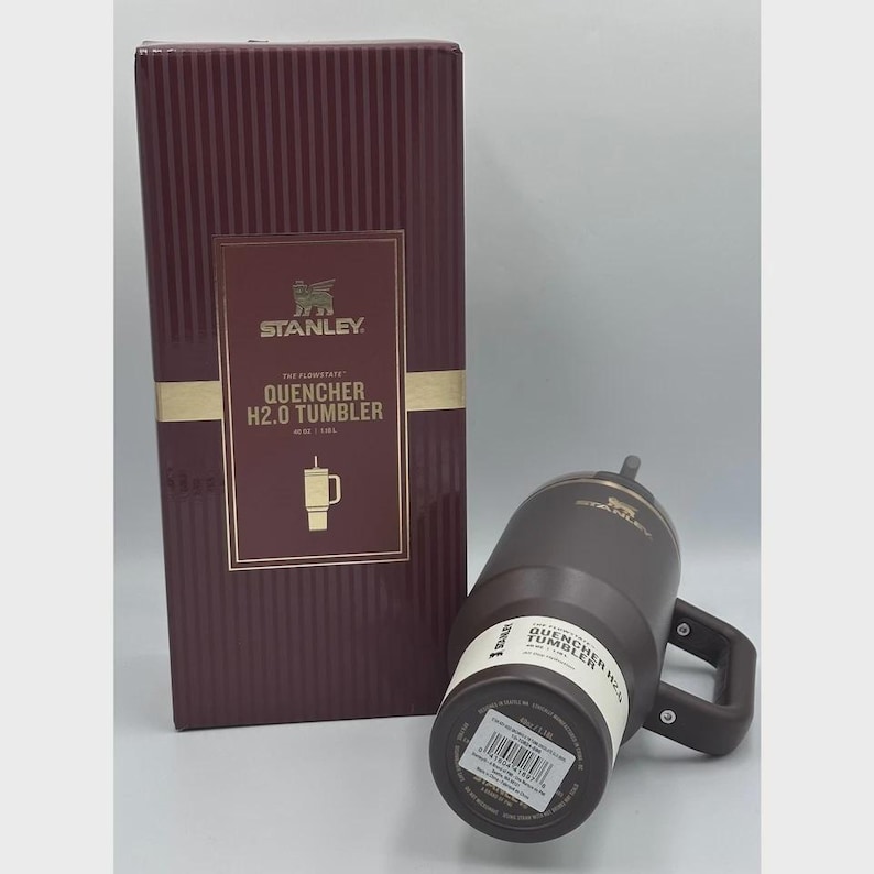 Peut inclure: Un gobelet Stanley Quencher H2.0 marron avec une poign&eacute;e et une bo&icirc;te bordeaux assortie. La bo&icirc;te pr&eacute;sente le logo Stanley et des informations sur le produit. Le gobelet est con&ccedil;u pour les boissons froides.