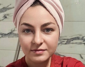 Può includere: Un asciugamano per capelli rosa chiaro avvolto attorno alla testa. La persona indossa una maglietta rossa. Lo sfondo è un bagno con piastrelle con motivo marmoreo.