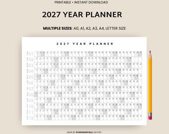 May include: A white 2027 year planner with a grid layout, featuring months and days. The text "2027 YEAR PLANNER" is at the top. A yellow pencil with a pink eraser rests on the right. The planner is available in multiple sizes.
