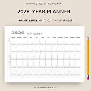 Könnte beinhalten: Ein weißer 2026 Jahresplaner mit einem Raster für jeden Monat. Der Text "2026 YEAR PLANNER" steht oben, darunter sind Größenoptionen aufgeführt. Rechts ist ein gelber Bleistift mit rosa Radiergummi.