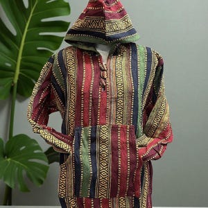 May include: A colorful hooded pullover with a front pocket. The garment features vertical stripes in red, green, blue, and gold, with patterned accents. The hood is also patterned. The pullover is displayed on a mannequin.