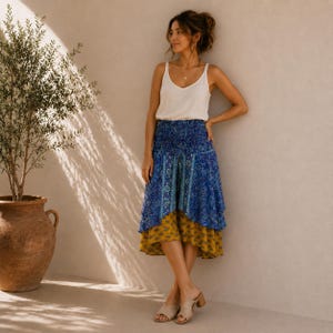 May include: A white sleeveless V-neck camisole top paired with a layered midi skirt featuring a blue and white floral print on the top tier and a mustard yellow patterned print on the bottom tier, finished with a smocked elasticized waistband.