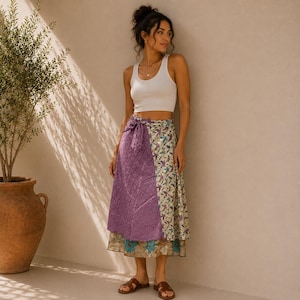 May include: A white tank top paired with a midi-length wrap skirt featuring a purple quilted panel on one side and a cream-colored panel with a blue and green floral and bird pattern on the other, finished with a tie closure at the waist.