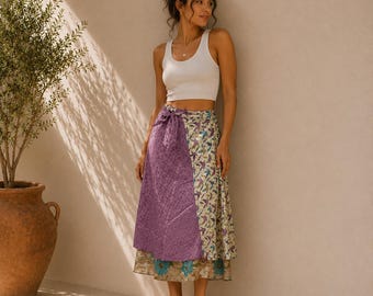 May include: A white tank top paired with a midi-length wrap skirt featuring a purple quilted panel on one side and a cream-colored panel with a blue and green floral and bird pattern on the other, finished with a tie closure at the waist.