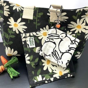 May include: A black tote bag, wallet, and small pouch with a white daisy floral pattern. The wallet has the text "Polish Rabbit". A small carrot decoration and a keychain with a heart charm are also present.