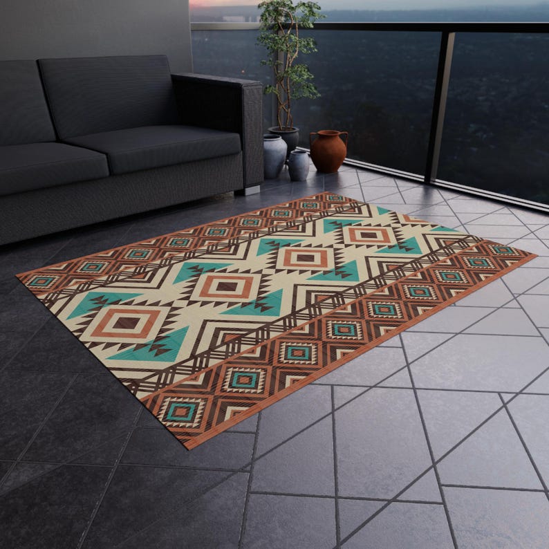 May include: Rectangular outdoor rug with a geometric pattern in shades of brown, teal, and cream. The rug features a border with diamond shapes and a central design of triangles and squares. The rug is placed on a tiled surface.