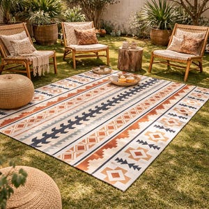 May include: An outdoor scene featuring a large rectangular rug with a geometric pattern in shades of cream, orange, and navy blue. Wicker chairs with cushions and a woven ottoman are arranged on the grass, creating a cozy seating area.