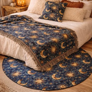 May include: A bedroom scene with a bed dressed with a navy blue blanket and cushion set, decorated with a celestial sun and moon design. A matching round rug is on the floor. The blanket has a fringed edge.