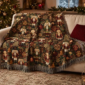 May include: A woven throw blanket featuring a repeating pattern of nutcracker figures, golden bells, and snowflakes on a dark green background. The blanket has a fringed edge and displays a detailed tapestry-style design with red and gold accents.