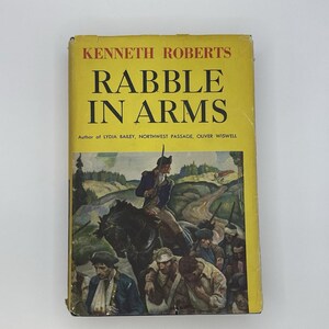 May include: A hardcover book titled Rabble in Arms by Kenneth Roberts with a yellow dust jacket. The cover features a historical illustration of a soldier on horseback leading a group of injured individuals through a landscape with trees and hills.