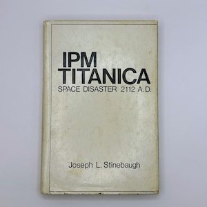 May include: A rectangular book with a cream-colored cover featuring black text that reads IPM TITANICA SPACE DISASTER 2112 A.D. and the author name Joseph L. Stinebaugh at the bottom, enclosed within a thin black rectangular border line.