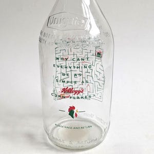 Può includere: Bottiglia di latte in vetro trasparente con un disegno stampato. Il disegno include un labirinto, il testo "WHY CAN'T EVERYTHING BE AS SIMPLE AS Kellogg's CORN FLAKES?" e il logo Kellogg's. La bottiglia ha anche il testo "PLEASE RINSE AND RETURN".