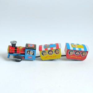 May include: A vintage toy train with three cars. The engine is blue, red, and gold, with the number 7035 on the side. The cars are yellow and red, each with illustrations of children and the word "DREAMLAND".