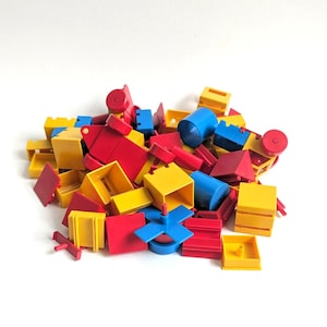 Puede incluir: Un montón de bloques de construcción de plástico de colores rojo, amarillo y azul. Los bloques tienen varias formas, incluyendo cubos, rectángulos y cilindros. Algunos bloques tienen agujeros o clavijas para conectar. Los bloques están esparcidos sobre una superficie blanca.