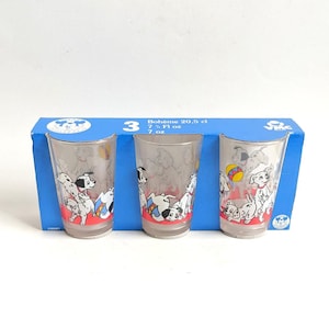 Puede incluir: Juego de tres vasos transparentes con diseños de cachorros dálmatas. Cada vaso tiene una base roja y está decorado con cachorros juguetones. Los vasos se muestran en una caja azul con el texto "Boheme 20,5 cl 7 fl oz".