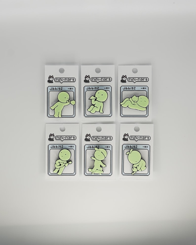 Puede incluir: Seis dijes Jibbitz verdes, cada uno con una figura de dibujos animados en diferentes poses. Los dijes est&aacute;n adheridos a tarjetas blancas con el texto "Mini-Mart" y "Jibbitz -ox". El fondo es blanco.