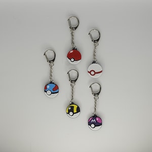 May include: Six keychains with round, colourful designs. Each keychain features a different design, including red and white, blue and white, yellow and black, and purple and white. The keychains have silver-coloured chains and key rings.