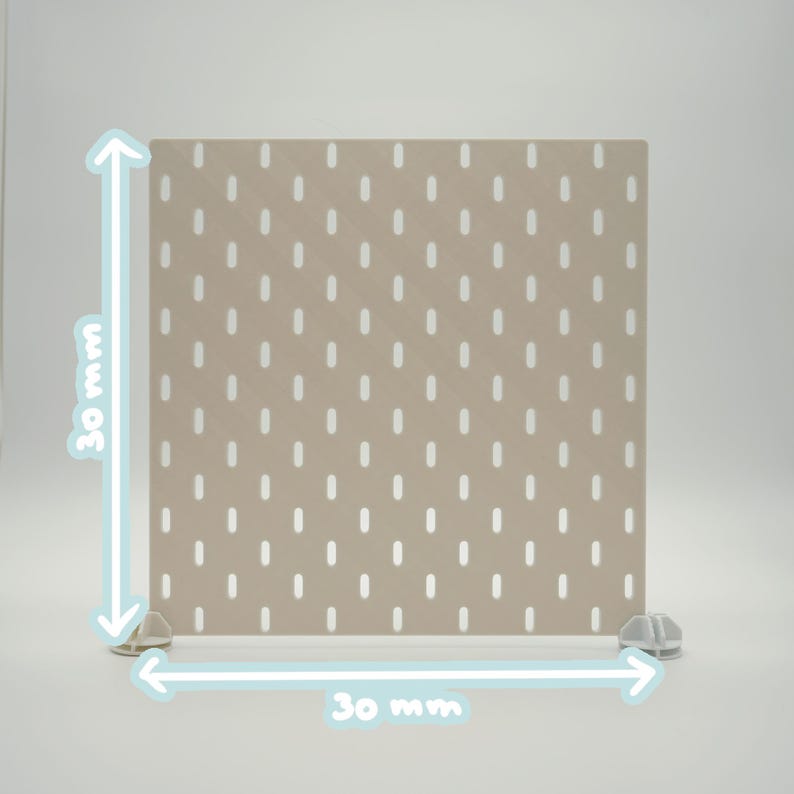 May include: A square beige pegboard panel featuring a grid of vertical oval slots. The panel is supported by two small white plastic feet at the base. The image includes light blue arrows and text indicating dimensions of 30 mm by 30 mm.