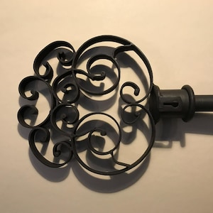 Puede incluir: Una decoración de pared en forma de llave de metal negro con intrincados detalles de volutas.