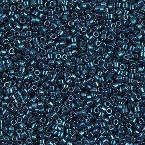 May include: A close-up shot of a pile of small, dark teal seed beads. The beads are cylindrical with a hole running through the center. The surface of the beads has a metallic sheen, reflecting light. The beads are scattered, creating a textured surface.
