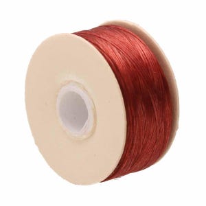 May include: A spool of vibrant red cord wrapped around a circular beige cardboard core. The cord features a smooth, slightly reflective texture and is wound tightly in multiple layers across the width of the spool, showing a consistent deep red hue.