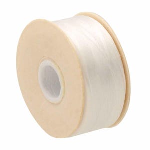 May include: A spool of white cord wrapped around a light beige plastic core. The cord is thin and translucent, wound tightly in multiple layers around the central cylinder, creating a smooth, cylindrical shape with a hollow center hole.