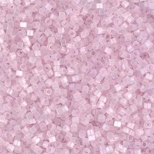 May include: A close-up view of a pile of small, light pink seed beads. The beads are cylindrical with a hole running through the center. The beads are scattered, creating a textured surface. The color is a soft, pastel pink.