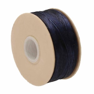 May include: A spool of dark navy blue cord wrapped around a circular beige cardboard core. The cord has a smooth, slightly shiny texture and is wound tightly in multiple layers around the center of the spool, which features a white plastic ring.