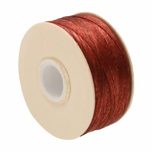 May include: A spool of dark red cord wrapped around a circular beige plastic core. The cord has a textured, fibrous appearance and is wound tightly in multiple layers around the center of the spool, which features a hollow circular opening.