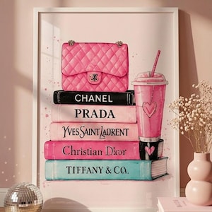 Peut inclure: Une impression d'art encadrée représentant une pile de cinq livres avec les noms CHANEL, PRADA, YVES SAINT LAURENT, Christian Dior et TIFFANY & CO. Un sac à main rose matelassé et une boisson glacée rose avec un cœur sont posés dessus.