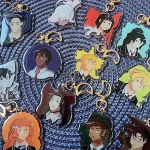 Könnte beinhalten: Eine Sammlung von zwölf Acryl-Schlüsselanhängern mit illustrierten Anime-Charakteren in Schuluniformen, die jeweils an einem goldfarbenen Verschluss in Form eines Halbmonds befestigt sind. Die Figuren haben unterschiedliche Haarfarben und Ausdrücke vor farbigen Hintergründen.