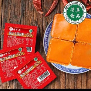 May include: An overhead shot features red packaging of Chongqing hot pot base, alongside four square, orange-colored blocks on a blue and white plate. The packaging includes Chinese text and a green Halal food logo. Dried red chilies are visible.