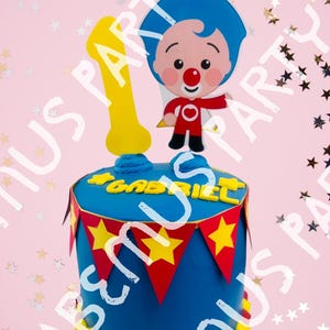 Pode incluir: Um bolo de aniversário azul decorado com uma personagem de desenho animado, um grande número um amarelo e o nome "GABRIEL" em letras amarelas. O bolo é adornado com bandeiras de bandeirola vermelhas e amarelas e uma borda amarela e vermelha.