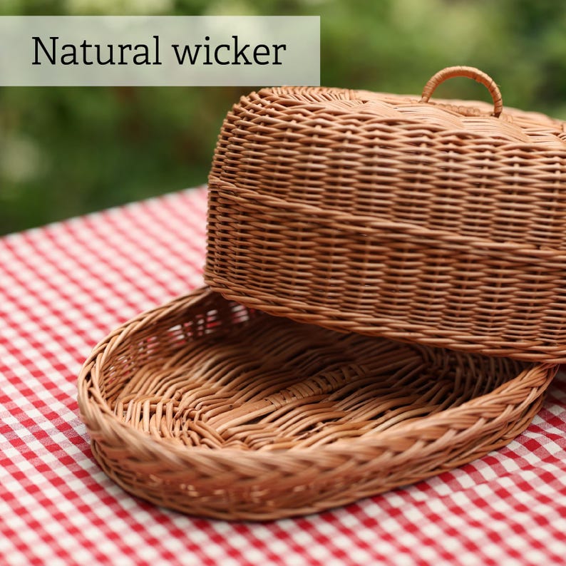 Op de afbeelding: Een natuurlijke rieten mand met deksel, geplaatst op een rood-wit geruite tafelkleed. Het deksel heeft een handvat. De tekst "Natural wicker" is zichtbaar.