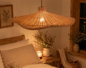 May include: A wide, flat, woven rattan pendant light fixture with a natural tan color, suspended from a brown twisted cord. The shade features an organic, wavy edge and a tight, intricate weave pattern that allows light to diffuse through the material.