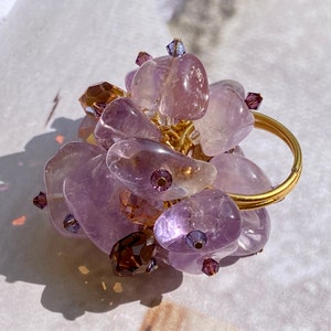 May include: A gold ring with a cluster of amethyst stones and small glass beads. The ring is made with wire wrapped around the stones.