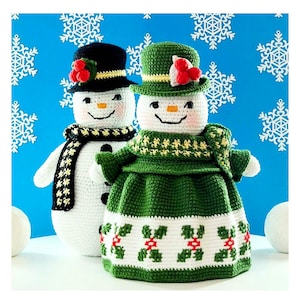 May include: Two handmade crochet snowmen. One snowman wears a black top hat and a black and white scarf. The other snowman is dressed in a green dress and hat with holly accents. Both snowmen have smiling faces and are set against a blue snowflake background.