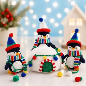 May include: Three crocheted penguin figurines and a white crocheted igloo. The penguins have black and white bodies, orange beaks, and wear colorful striped scarves and hats. A string of small, multi-colored crocheted lights drapes over the igloo.
