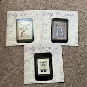 May include: Three cross-stitch patterns from Mirabilia, each featuring a different design. The first pattern shows a fairy with red flowers, the second shows two women in gowns, and the third shows a woman with a lantern.