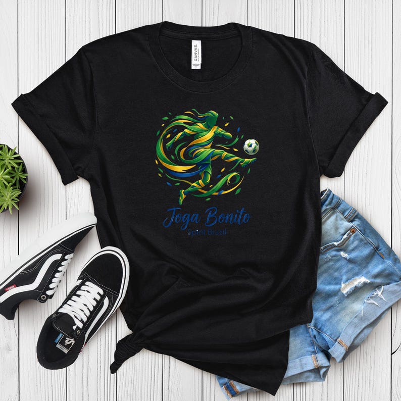 K&ouml;nnte beinhalten: Schwarzes T-Shirt mit einer dynamischen Grafik eines Fu&szlig;ballspielers in Aktion, mit gr&uuml;nen, gelben und blauen Akzenten. Der Text "Joga Bonito" ist in blauer Schrift geschrieben. Das T-Shirt wird mit Jeansshorts und schwarzen Turnschuhen kombiniert.