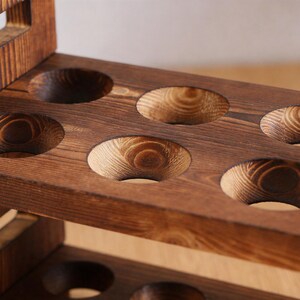 May include: A close-up of a wooden wine rack with six circular openings. The rack is made of dark brown wood with visible grain patterns. The openings are designed to hold wine bottles, showcasing a rustic and handcrafted aesthetic.
