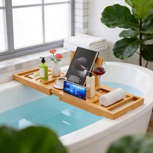 May include: A rectangular bamboo bathtub tray featuring a book stand, a smartphone slot, and dedicated compartments for a green soap dispenser, a white ceramic cup, a small vase with two pink roses, a wine glass, and a rolled white towel.