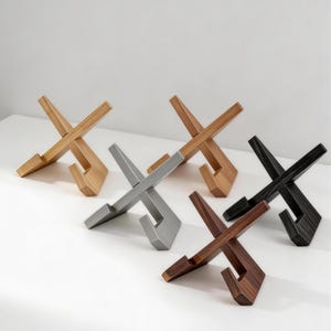 Op de afbeelding: Vijf X-vormige standaards gerangschikt in een groep, met verschillende afwerkingen waaronder licht hout, medium hout, donker hout, zwart en metallic zilver. Elke standaard bestaat uit twee in elkaar grijpende delen met een inkeping.