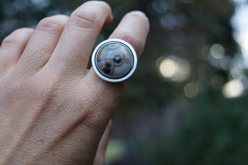 May include: A silver ring with a circular stone. The stone has a distinctive pattern of brown, green, and cream hues. The ring is set in a polished silver band.