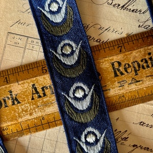 May include: Blue and green patterned ribbon with white accents. The ribbon has a repeating design of stylized eyes. The ribbon is lying on top of a wooden ruler with the words "York Arm" and "Repair" printed on it.