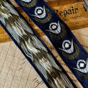 May include: Two blue and white patterned ribbon trims with a repeating design of stylized eyes. The ribbon trims are on a brown surface with a ruler and a piece of paper with the word "Repair" written on it.