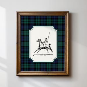 May include: Framed artwork featuring a black and white illustration of a polo player on horseback. The artwork is set against a green, navy, and black plaid pattern, framed in a dark wood. The artwork is mounted on a white background.