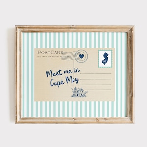 May include: A framed print featuring a vintage-style postcard design on a light blue and white vertical striped background. The postcard displays the text "Postcard" and "Meet me in Cape May" in dark blue, with a stamp showing the state of New Jersey.