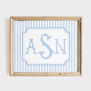 May include: A framed print featuring a light blue monogram with the letters "ASN" in a decorative font. The monogram is set against a white background within a light blue and white striped border. The frame is a light brown color.
